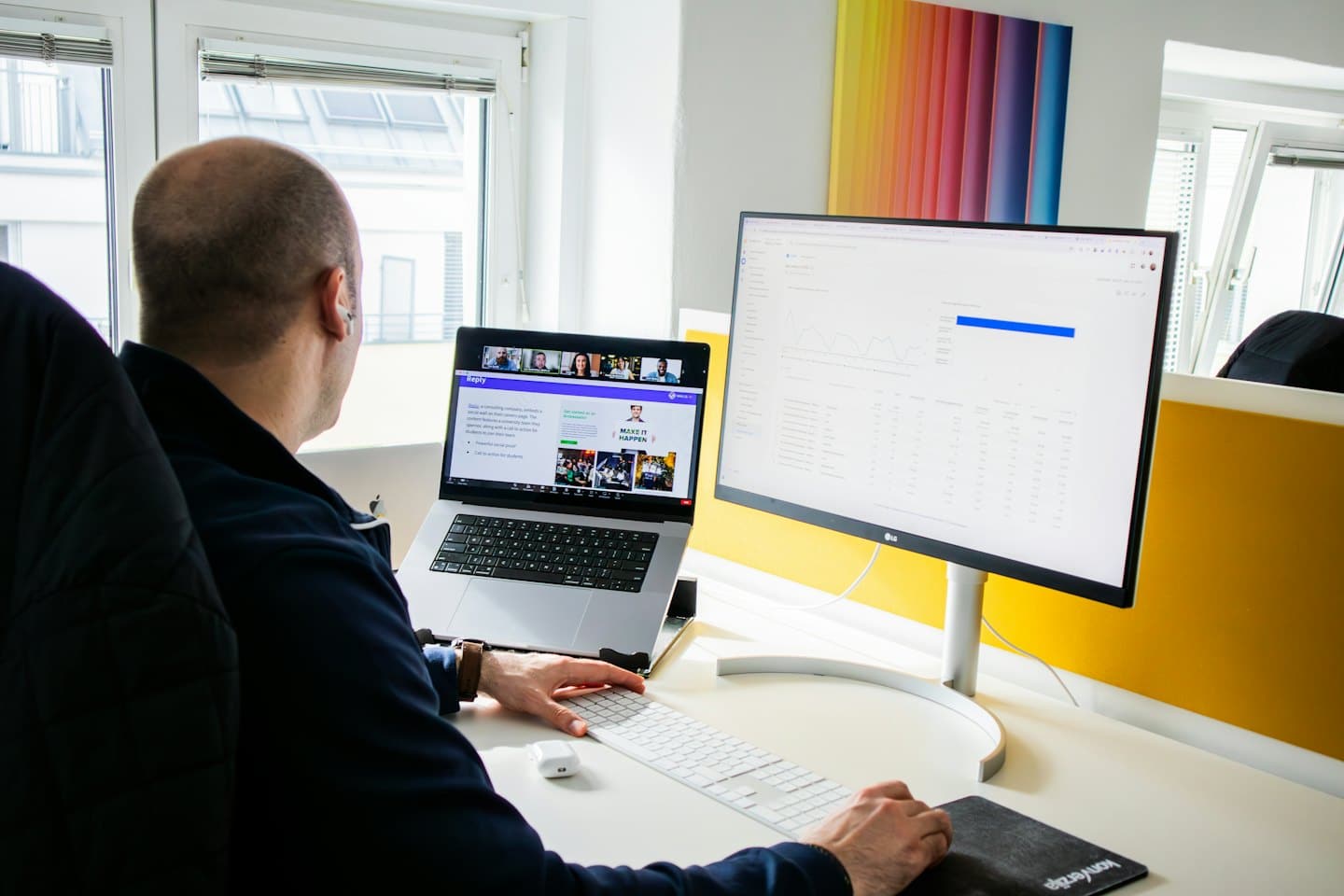 Man works on laptop and monitor in modern office.